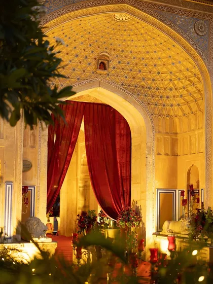 The intricate, illuminated archways of Chomu Palace at night, with rich red curtains adding a touch of drama. The venue itself becomes a key character in the wedding's narrative.
