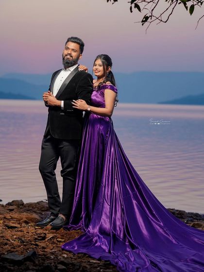 A picture of pure elegance by the water. The rich purple satin of this trail gown contrasts beautifully with the serene landscape, creating a regal look for this couple's pre-wedding shoot.