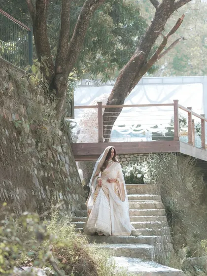 A beautiful wide shot of the bride descending a rustic staircase at her riverside wedding venue in Rishikesh, a moment of quiet elegance.
