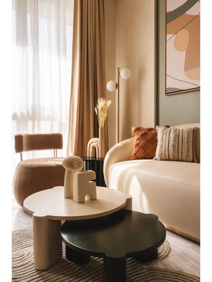 The nesting coffee tables feature organic shapes that complement the sculpted furniture. This detail, along with the curated decor, adds to the apartment's overall aesthetic of refined elegance and thoughtful design.