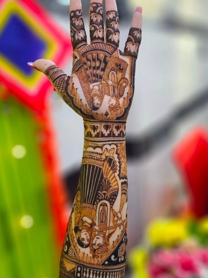 A single hand raised to showcase a detailed portrait design. The background decor hints at the festive mehndi ceremony atmosphere.
