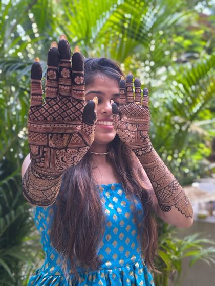 A happy bride showing off her full bridal mehendi. The design extends up to the elbows, featuring a mix of traditional Indian patterns for a complete look.