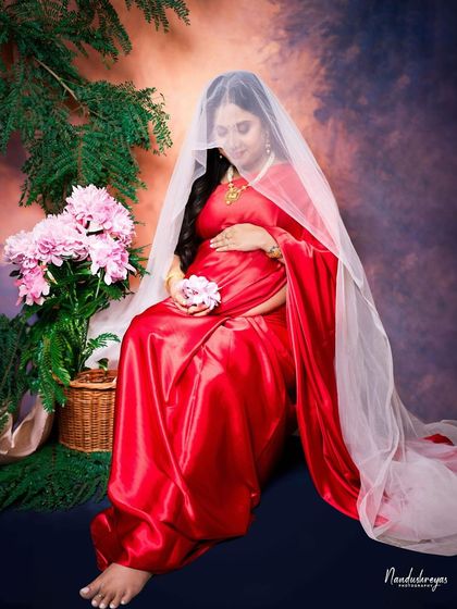 A wider shot of the veiled portrait, showing more of the beautiful red saree and the floral props, creating a complete, artistic scene.