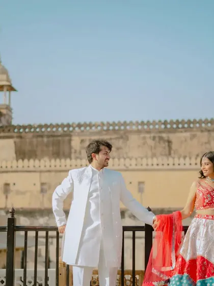 A classic pose against the backdrop of a Jaipur fort. The couple's traditional outfits in white and red create a striking contrast, perfect for a timeless pre-wedding album.