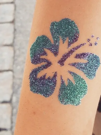 A hibiscus flower tattoo with a green and purple glitter blend. This tropical design is perfect for summer parties or a Moana-themed event.