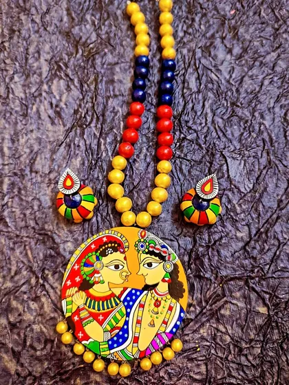 This piece is a celebration of love, featuring a hand-painted depiction of Radha and Krishna in the Madhubani style. I use a vibrant palette on a circular terracotta pendant, complemented by colorful beads. It’s a piece of art that tells a timeless story.