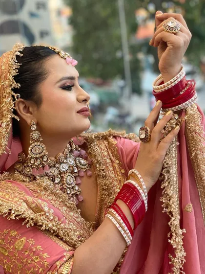A classic bridal pose showing the beautiful details of her hands, bangles, and rings. The makeup is kept elegant to complement the heavy jewelry and ornate outfit.