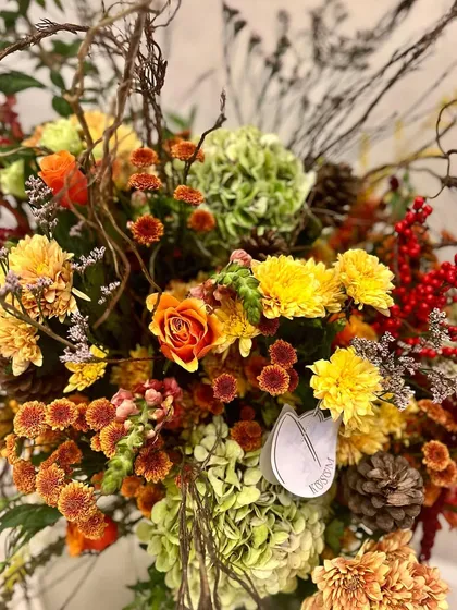 A close-up on the colours of autumn. The combination of yellow chrysanthemums, orange snapdragons, red ilex berries, and rustic pinecones creates a beautiful, warm, and textured design.