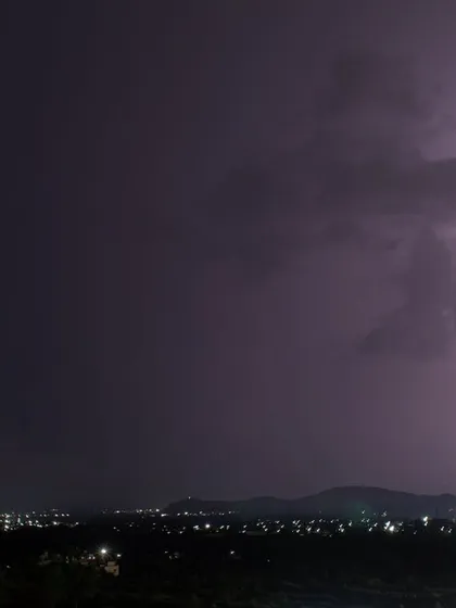 A bright, single bolt of lightning strikes down behind a hill on the outskirts of Pune.