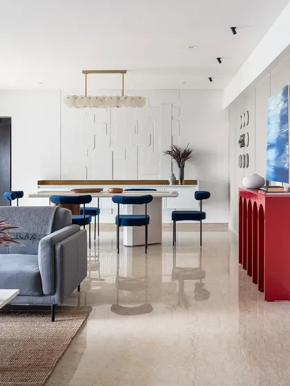 A glimpse into an open-plan living and dining area where modern design meets vibrant personality. The striking red console and rich blue velvet chairs add a bold splash of color, showcasing how we tailor each space to reflect our client's unique style while maintaining a cohesive, elegant flow.