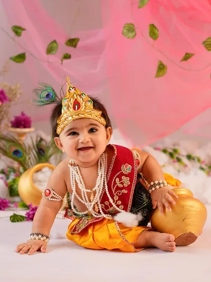 This little Krishna, with his sweet smile and traditional attire, leans against a golden pot. Our Janmashtami sessions are filled with authentic props to make the theme come alive.