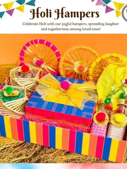 A bright and colorful Holi hamper in a rainbow-striped box. It contains beautifully packaged sweets and drinks, adorned with yellow ribbons and decorative wheels, perfectly capturing the joyful spirit of the festival.