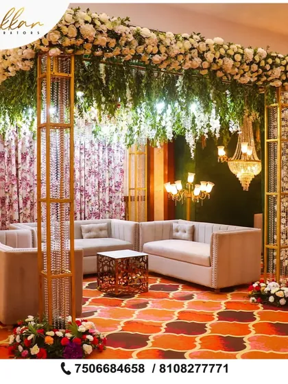 A chic lounge area for guests at a reception. The setup features modern sofas under a canopy of flowers and crystal-adorned pillars, blending comfort with high-end design.