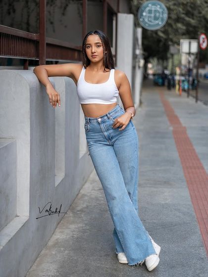 A classic street style pose, leaning against a concrete wall. The clean lines of the architecture contrast with the relaxed outfit, creating a balanced and modern fashion portrait.