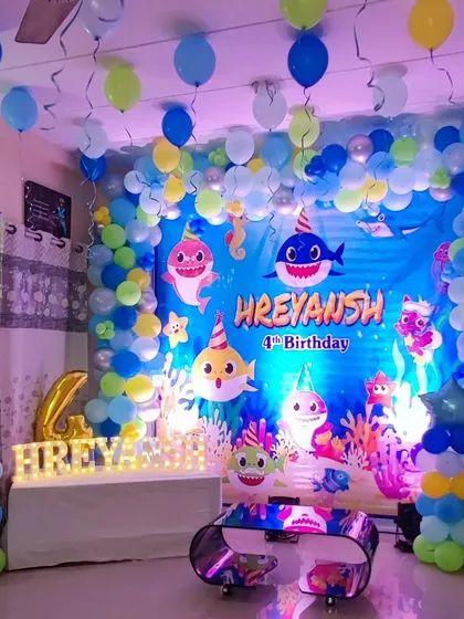 An underwater adventure with this "Baby Shark" themed fourth birthday party. The setup includes a large ocean-themed backdrop with the Baby Shark family, framed by a blue, yellow, and green balloon arch to create a fun, aquatic feel.