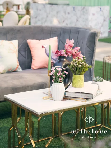 A small table setting within 'The Conservatory', showcasing the mix of modern furniture and soft, floral details.