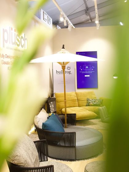 A creatively framed shot of the Plüsch booth, seen through foliage. This perspective captures the inviting and layered nature of the space, with the yellow sofa providing a pop of color.