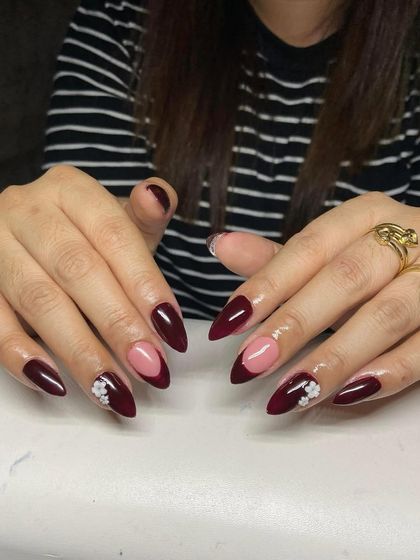 A deep maroon French manicure with a nude base and delicate white 3D flower accents. This design is sophisticated and perfect for special occasions.
