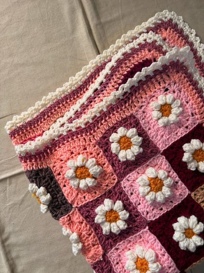 Another angle of the folded Daisy blanket, showing how the layers of crochet create a thick, warm, and cozy keepsake. The colors are chosen to create a warm and inviting palette.