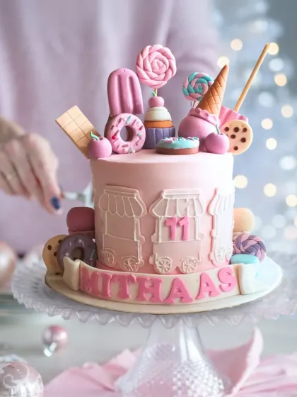 A sweet pink cake celebrating all things sweet, topped with fondant ice cream cones, lollipops, and donuts.