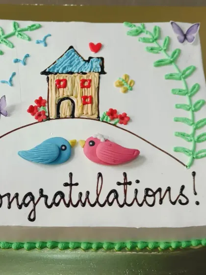 A sweet "Congratulations" cake celebrating a new home. The design features two lovebirds and a charming little house, all hand-piped with buttercream.