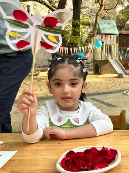 A girl proudly holds up the beautiful butterfly craft she made, with wings decorated with colorful flower petals.