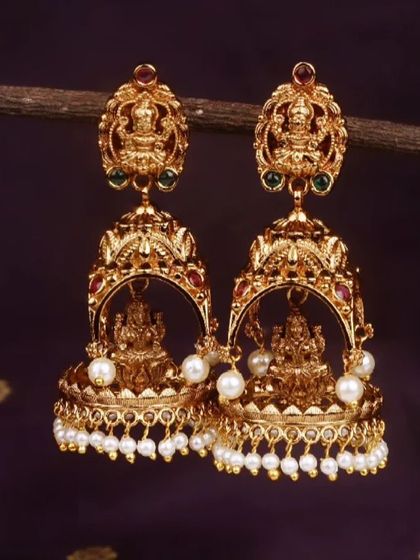 These traditional temple jhumkis have a matte gold finish and feature a beautiful Goddess Lakshmi motif. This pair is adorned with classic pearl drops, adding to their timeless elegance.