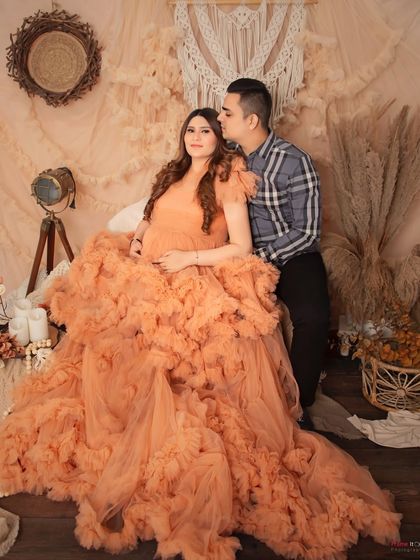 A stunning maternity portrait in a voluminous peach gown. The boho-chic setup with pampas grass and macrame adds a soft, earthy feel to the photograph.