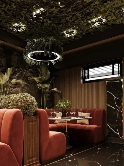A cozy booth seating area in a restaurant, featuring rich, rust-colored upholstery and a ceiling filled with hanging plants. The design combines dark marble, textured stone walls, and warm lighting to create an intimate, nature-inspired dining nook.