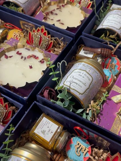 A close-up of another premium Diwali hamper, this time with a purple theme. It includes chamomile green tea, a decorative candle, and other festive items.