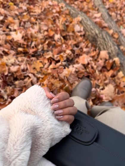 A detail shot focusing on my nails and clutch against a backdrop of fallen autumn leaves, capturing the seasonal aesthetic.