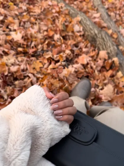 A detail shot focusing on my nails and clutch against a backdrop of fallen autumn leaves, capturing the seasonal aesthetic.