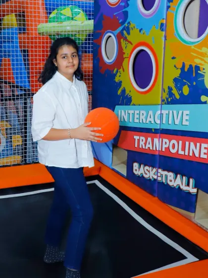 A girl holds a basketball in our interactive trampoline zone, ready for her next shot. The colorful wall adds to the vibrant and playful atmosphere.