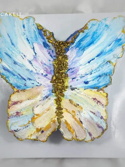 A butterfly-shaped cake decorated with an abstract, impressionistic painting style using buttercream. The gold details add a touch of elegance to this artistic chocolate truffle cake.