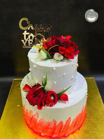 A vibrant two-tier cake for a 50th birthday celebration. This Red Velvet cake is decorated with a bold red brushstroke effect and beautiful fresh red flowers.