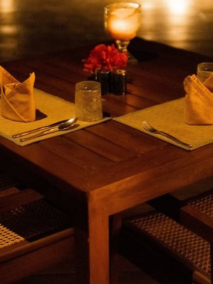 An intimate dinner setting by candlelight. The table is simply set for two, with folded napkins and a single flower, overlooking the pool for a romantic evening.