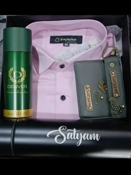 This gift hamper combines a pink shirt with a personalized grey wallet and keychain, a name-engraved bottle, and deodorant.