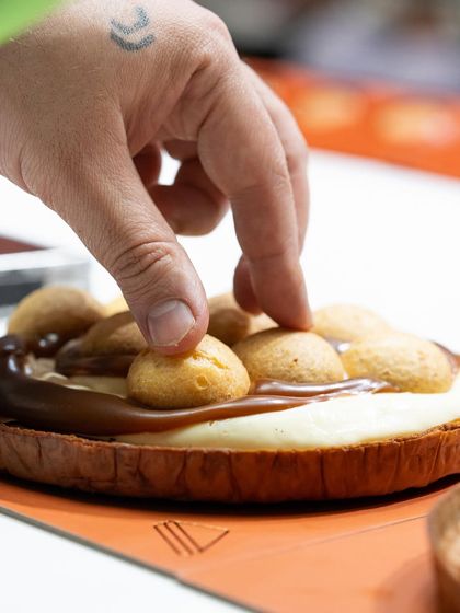 Assembling a classic St. Honoré tart, with choux buns placed carefully on a bed of cream.