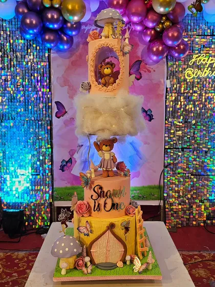 A magical fairy house cake for a first birthday, featuring a topsy-turvy design with teddy bears, mushrooms, and butterflies.