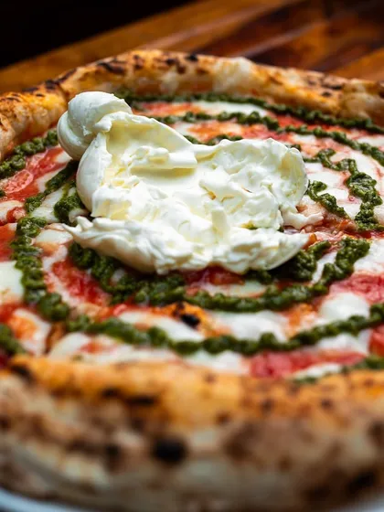 A full view of our Burrata Pesto masterpiece. A whole creamy burrata sits atop a swirl of vibrant pesto on our signature Neapolitan base. It's as extra and delicious as it looks.