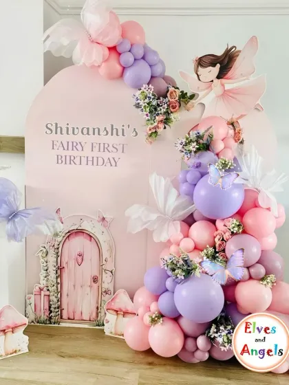 A whimsical fairy first birthday for Shivanshi. The decor featured a beautiful pink and purple balloon cascade flowing down a custom arch with a fairy door and butterfly details.