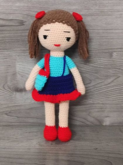 This doll is wearing a blue top and a red skirt, with a matching bag. She looks very smart.