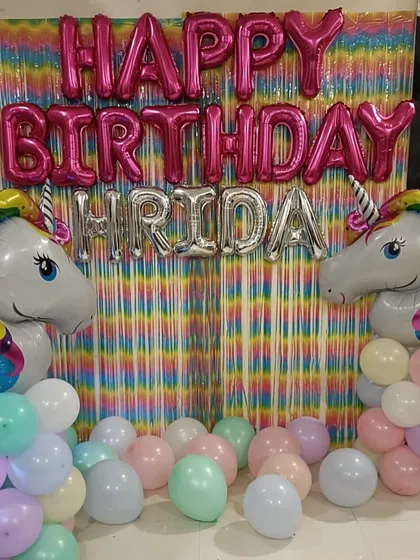 A magical unicorn-themed birthday party. We used a rainbow fringe curtain as the backdrop, flanked by large unicorn foil balloons and pastel balloon clusters, with the birthday girl's name spelled out in foil letters.