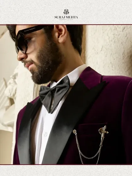 I work with luxurious fabrics to create statement pieces. This close-up highlights the rich texture of a wine-colored velvet tuxedo jacket, complete with a satin lapel and an elegant chain brooch, perfect for festive occasions and black-tie events.
