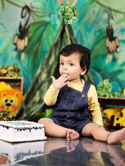 A baby boy in a jungle-themed cake smash curiously tastes the frosting from his finger before diving in.
