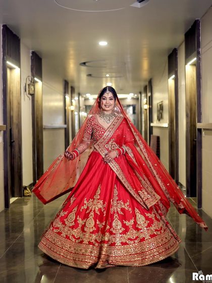 A full-length shot of the bride showing off her magnificent red lehenga with a wide, happy twirl in a hotel corridor.