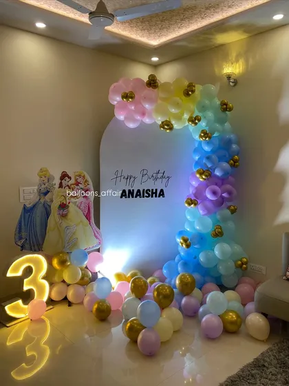 A dreamy Disney Princess theme for a 3rd birthday. This setup includes a pastel rainbow balloon arch, a large light-up number '3', and cutouts of Cinderella, Belle, and Aurora.