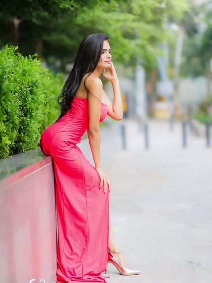A relaxed and elegant pose, leaning against a wall. The vibrant pink dress stands out beautifully in the urban environment.