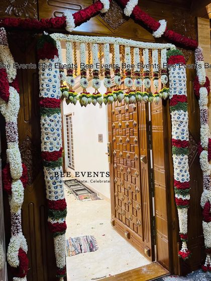 A beautifully decorated main door for a Gruha Pravesha. The elaborate 'thomala' is made with jasmine, rose petals, and sacred leaves, creating a grand and traditional welcome.