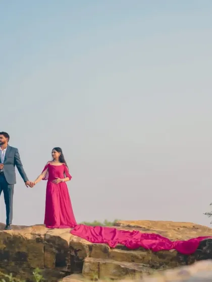 A romantic shot of the couple on a cliff edge. The soft trail of the rani pink gown drapes elegantly below them, adding to the fairytale feel.